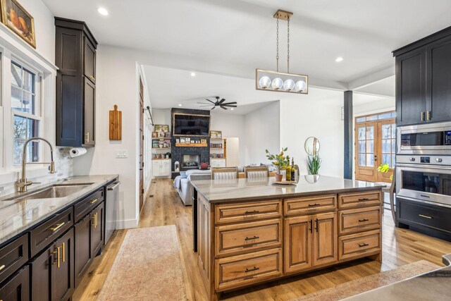 kitchen with a kitchen island, appliances with stainless steel finishes, sink, hanging light fixtures, and light stone counters