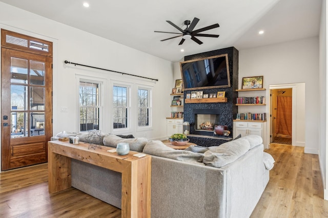 living room featuring ceiling fan, a stone fireplace, and light wood-type flooring