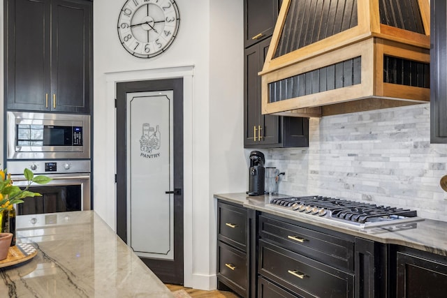 kitchen featuring stainless steel appliances, light stone countertops, exhaust hood, and backsplash