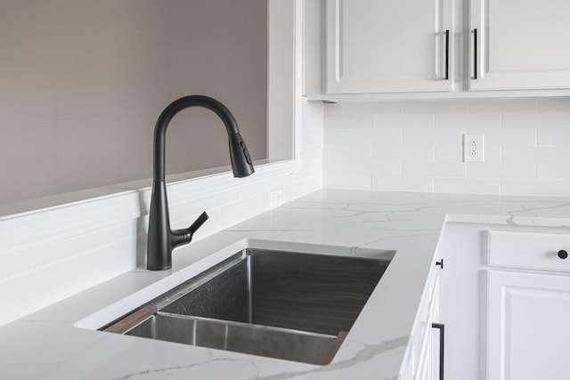 interior details featuring white cabinetry, light stone countertops, sink, and backsplash