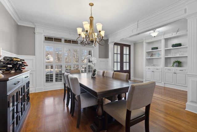 dining room featuring crown molding, dark wood-type flooring, built in features, and an inviting chandelier