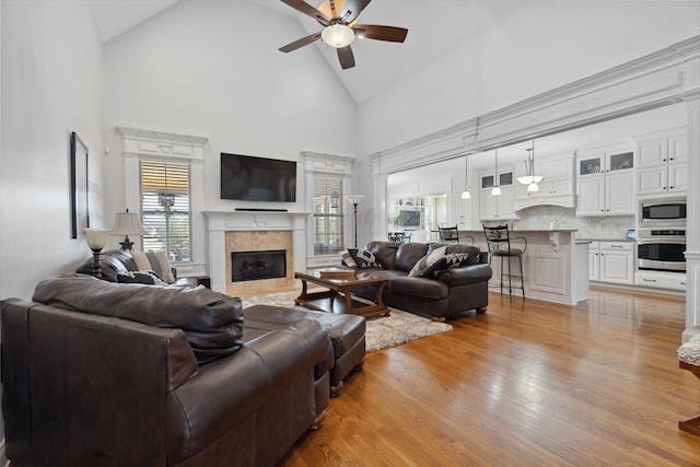 living room with ceiling fan, high vaulted ceiling, a tile fireplace, and light wood-type flooring