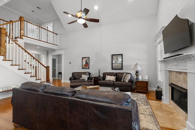 living room featuring a tiled fireplace, ornamental molding, high vaulted ceiling, and ceiling fan