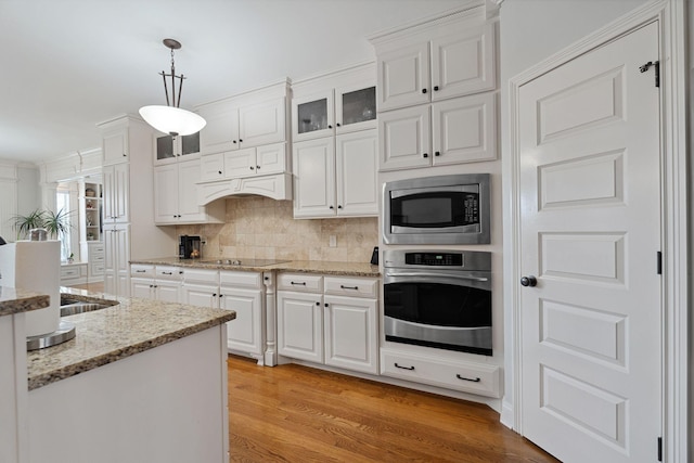 kitchen featuring white cabinetry, tasteful backsplash, hanging light fixtures, light hardwood / wood-style flooring, and appliances with stainless steel finishes