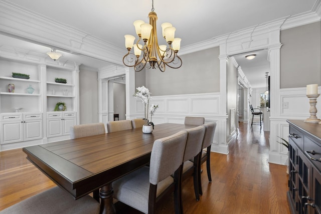 dining area with built in features, decorative columns, a notable chandelier, ornamental molding, and dark hardwood / wood-style flooring