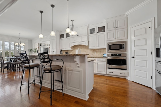 kitchen featuring pendant lighting, stone counters, white cabinetry, stainless steel appliances, and a center island