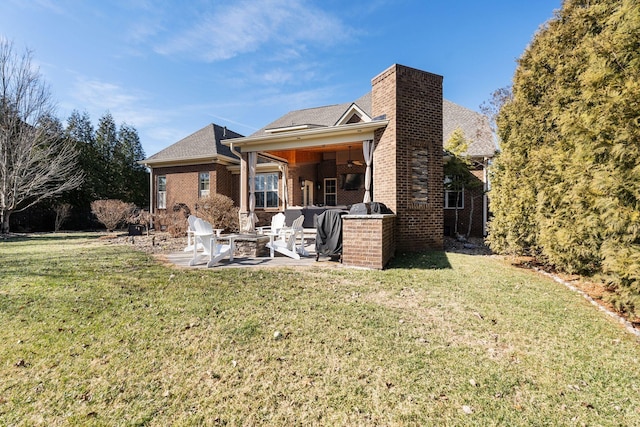 rear view of house with ceiling fan, a yard, a patio area, and a fire pit