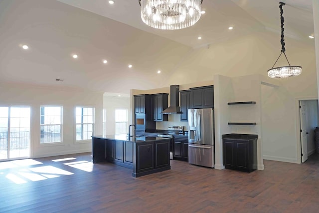 kitchen with stainless steel appliances, a chandelier, wall chimney range hood, and an island with sink