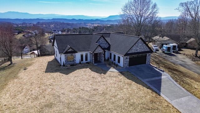 french country style house with an attached garage, a mountain view, stone siding, concrete driveway, and a front yard