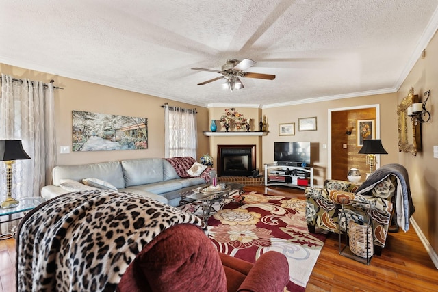 living room with crown molding, a textured ceiling, hardwood / wood-style flooring, ceiling fan, and a fireplace