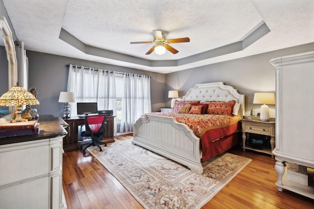 bedroom featuring a raised ceiling, hardwood / wood-style flooring, and a textured ceiling