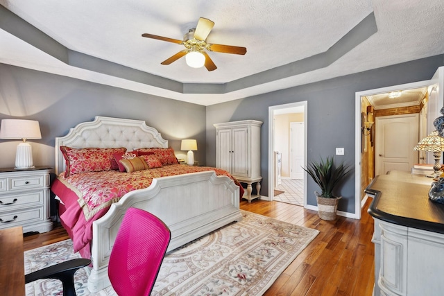 bedroom featuring ceiling fan, dark hardwood / wood-style flooring, a raised ceiling, and a textured ceiling