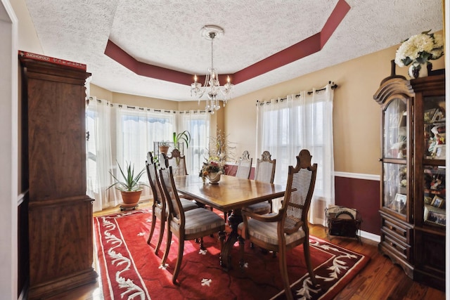 dining space featuring dark hardwood / wood-style flooring, a raised ceiling, a textured ceiling, and a notable chandelier