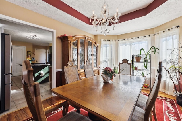 tiled dining room with a chandelier, a textured ceiling, and a tray ceiling