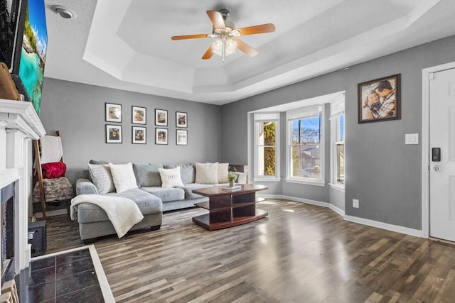 living room with dark wood-type flooring, a raised ceiling, and ceiling fan