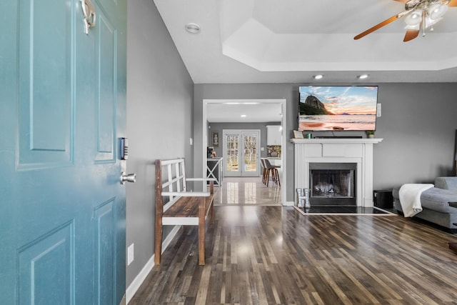 living room featuring a tray ceiling, dark wood-type flooring, french doors, and ceiling fan