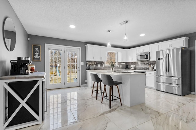 kitchen with a healthy amount of sunlight, appliances with stainless steel finishes, decorative light fixtures, and white cabinets