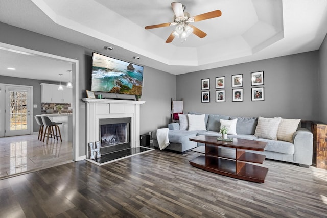 living room with hardwood / wood-style floors, a raised ceiling, and ceiling fan