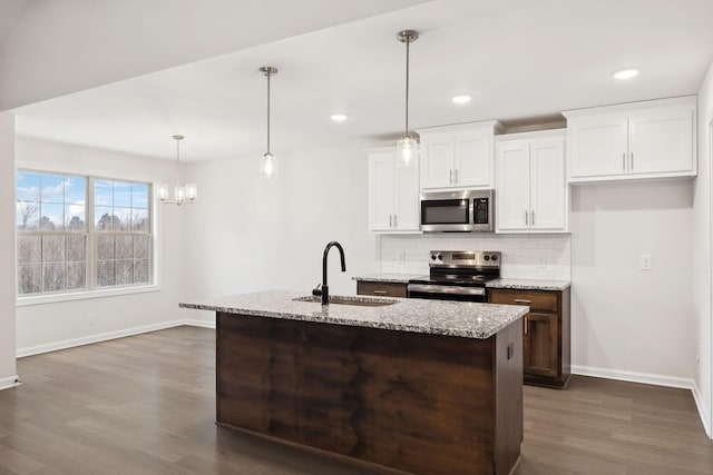 kitchen with sink, white cabinetry, decorative light fixtures, appliances with stainless steel finishes, and a kitchen island with sink