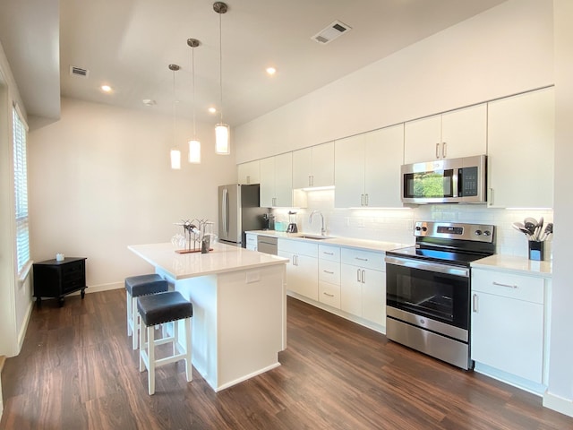 kitchen featuring sink, appliances with stainless steel finishes, white cabinetry, a kitchen island, and decorative light fixtures