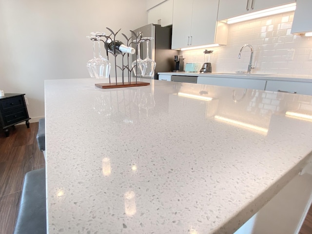 interior details with tasteful backsplash, sink, stainless steel fridge, white cabinets, and light stone counters