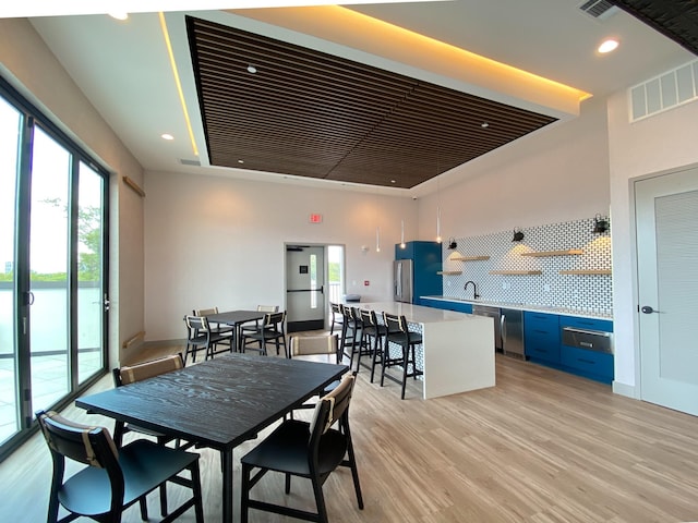 dining space featuring sink, light hardwood / wood-style floors, a raised ceiling, and a water view