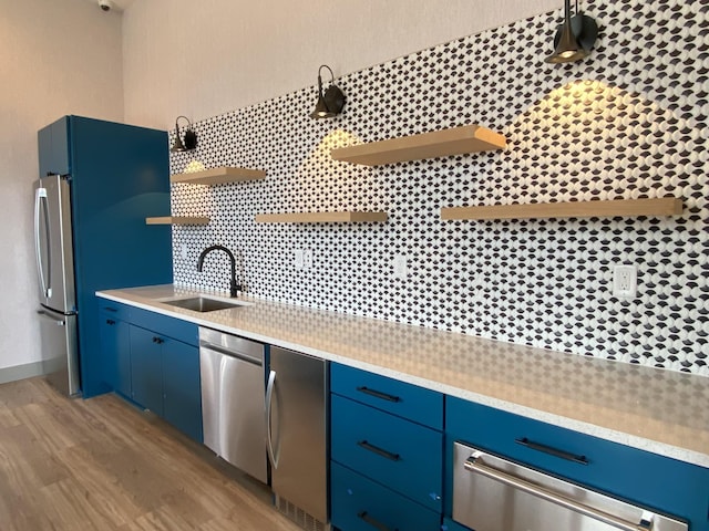 kitchen with blue cabinetry, stainless steel appliances, sink, and light hardwood / wood-style flooring