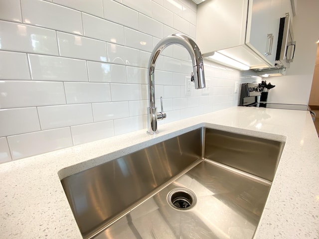 room details with white cabinets, light stone countertops, sink, and backsplash