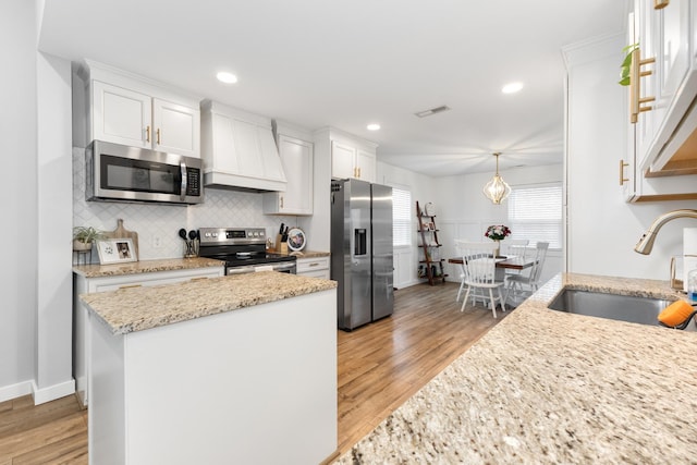 kitchen featuring wall chimney range hood, sink, white cabinets, and appliances with stainless steel finishes