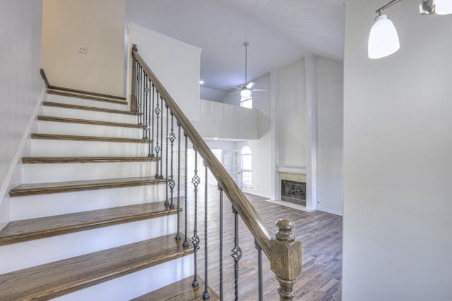 stairway with ceiling fan, high vaulted ceiling, hardwood / wood-style floors, and a tile fireplace