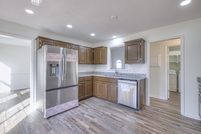 kitchen with stainless steel appliances, sink, light stone counters, and light hardwood / wood-style floors