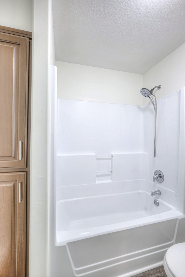 bathroom with shower / bathing tub combination, toilet, and a textured ceiling