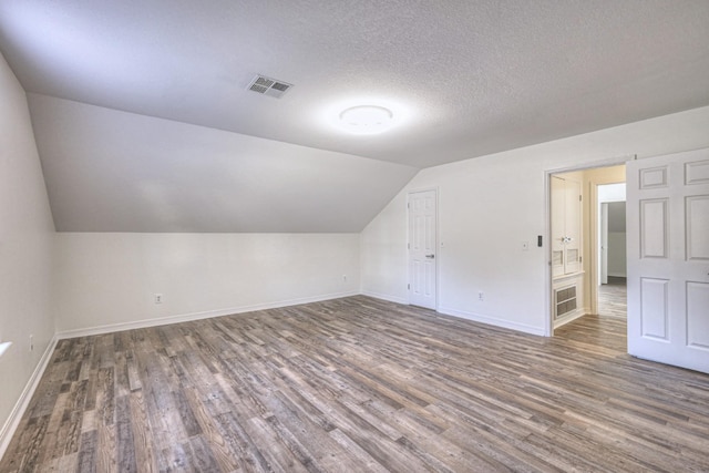 additional living space with dark hardwood / wood-style flooring, vaulted ceiling, and a textured ceiling