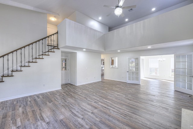 unfurnished living room with wood-type flooring, ceiling fan with notable chandelier, and a high ceiling