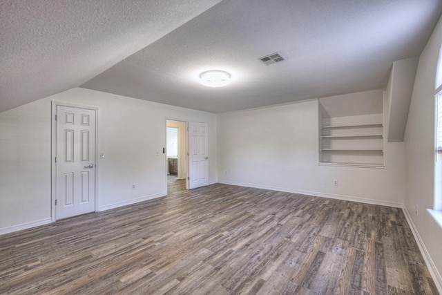 bonus room featuring dark wood-type flooring, built in shelves, and a textured ceiling