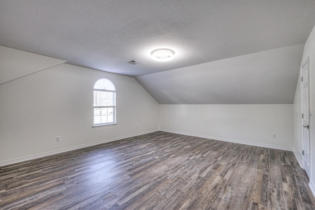 additional living space with lofted ceiling, dark wood-type flooring, and a textured ceiling