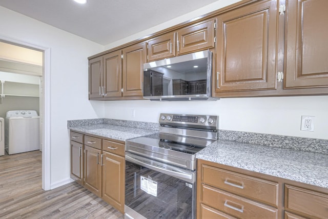 kitchen featuring appliances with stainless steel finishes, washing machine and dryer, and light wood-type flooring