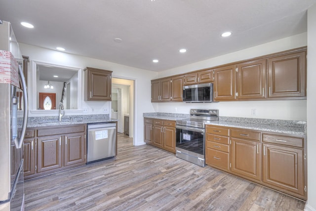 kitchen with appliances with stainless steel finishes, sink, light stone counters, and light hardwood / wood-style floors