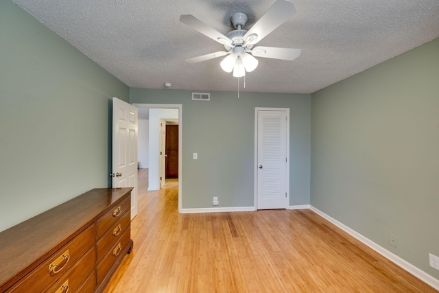 unfurnished bedroom featuring ceiling fan, a textured ceiling, light hardwood / wood-style floors, and a closet