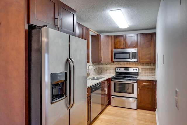 kitchen with appliances with stainless steel finishes, tasteful backsplash, sink, light stone counters, and light hardwood / wood-style flooring