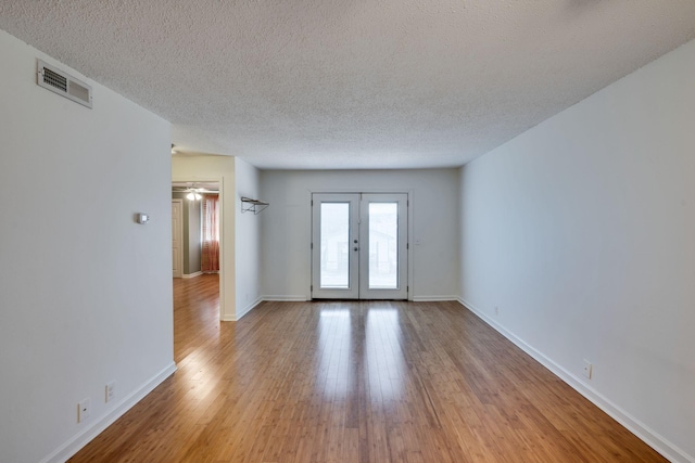 unfurnished room featuring a textured ceiling, light hardwood / wood-style floors, and french doors