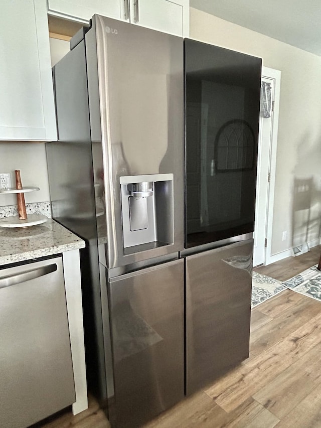 kitchen with white cabinetry, stainless steel appliances, light hardwood / wood-style floors, and light stone counters