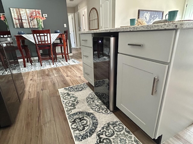 kitchen featuring hardwood / wood-style floors, white cabinets, wine cooler, a center island, and light stone countertops