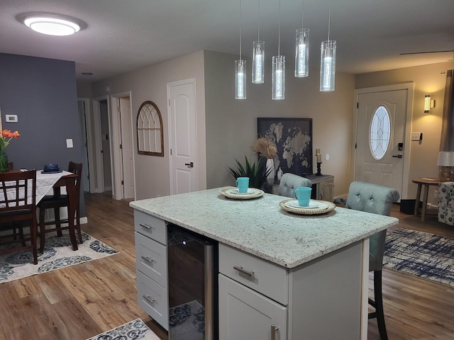 kitchen featuring decorative light fixtures, a center island, beverage cooler, hardwood / wood-style floors, and white cabinets
