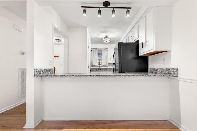 kitchen with black refrigerator, white cabinetry, light stone countertops, and light wood-type flooring