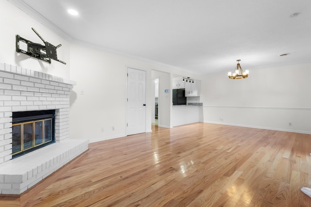 unfurnished living room with crown molding, a chandelier, a brick fireplace, and light wood-type flooring