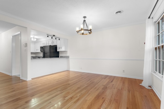 unfurnished living room featuring crown molding, a notable chandelier, and light wood-type flooring