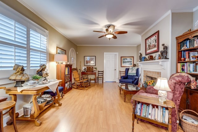 living area featuring crown molding, ceiling fan, light hardwood / wood-style floors, and a tile fireplace