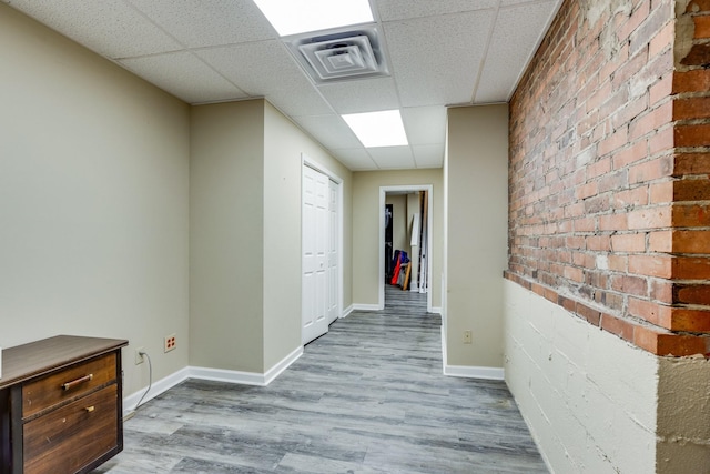 hallway featuring brick wall, hardwood / wood-style floors, and a drop ceiling