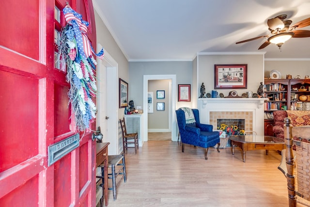 foyer with crown molding, a fireplace, ceiling fan, and light wood-type flooring